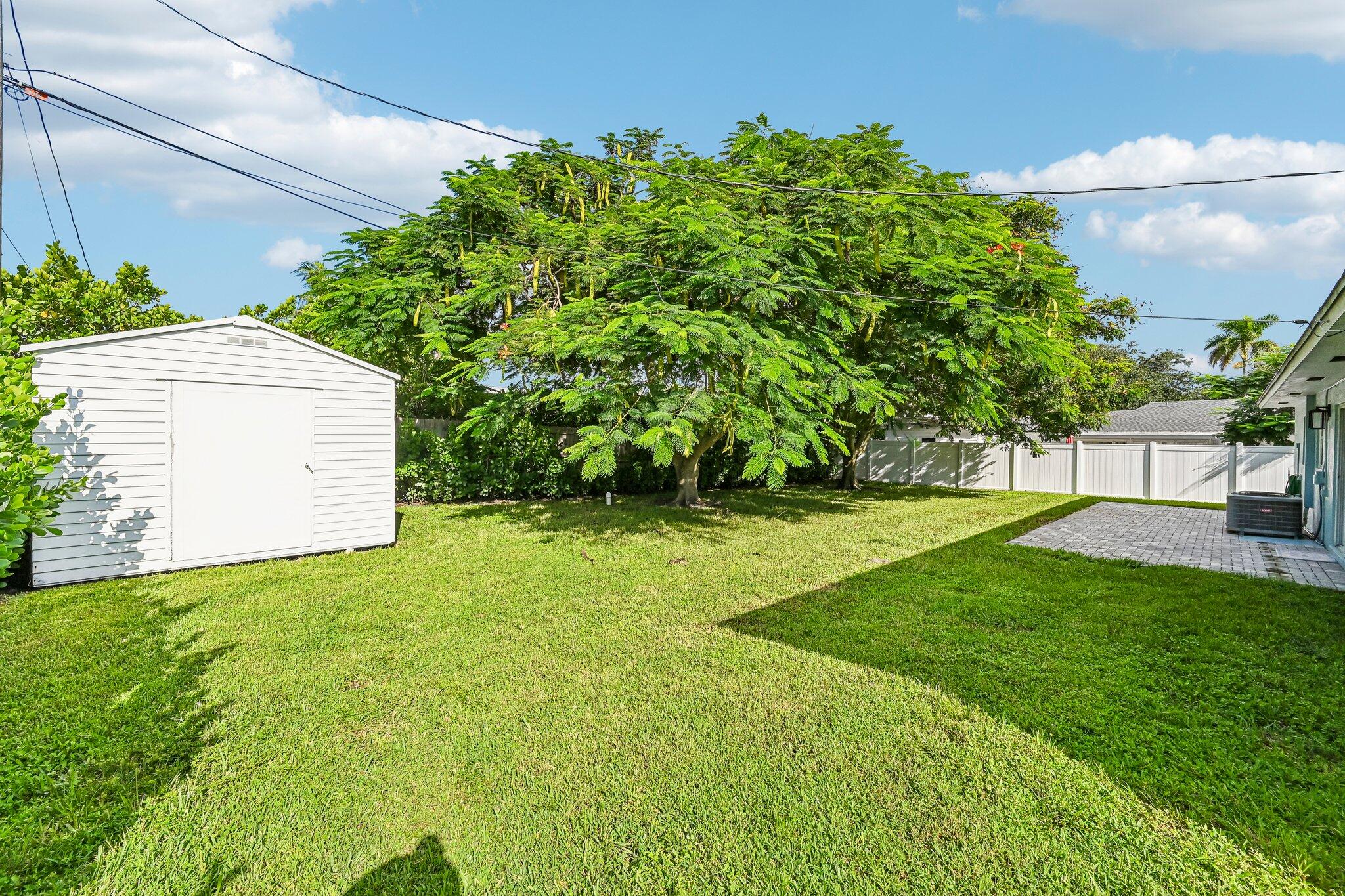 Backyard with a white storage shed, mature shade trees, lawn, and paved patio.