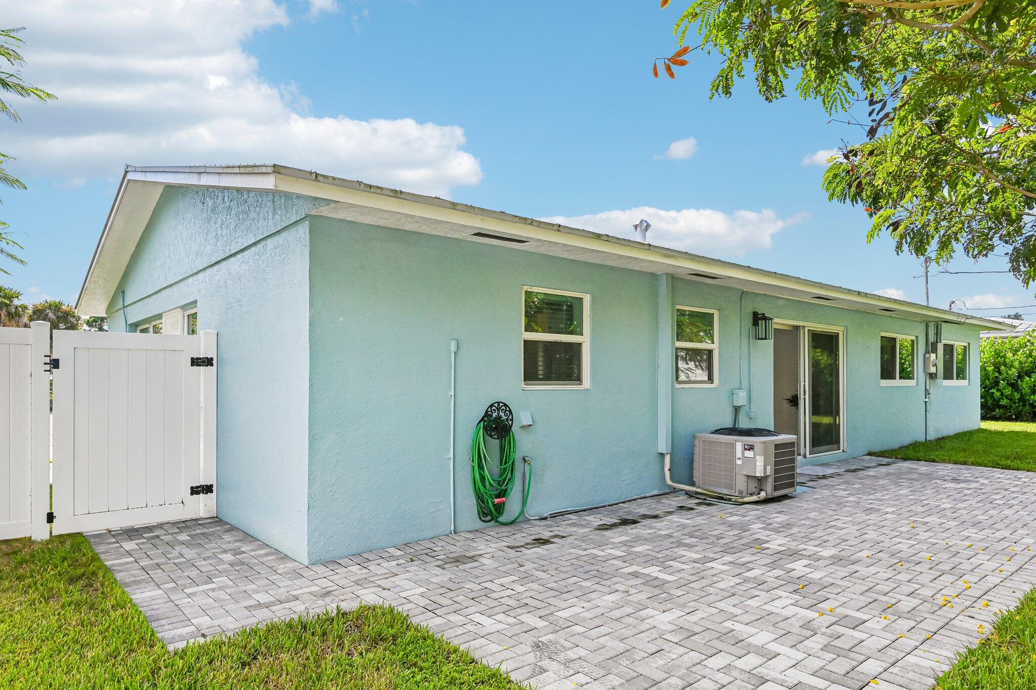 Light blue home exterior with a white gate, paved patio, and outdoor air-conditioning unit.