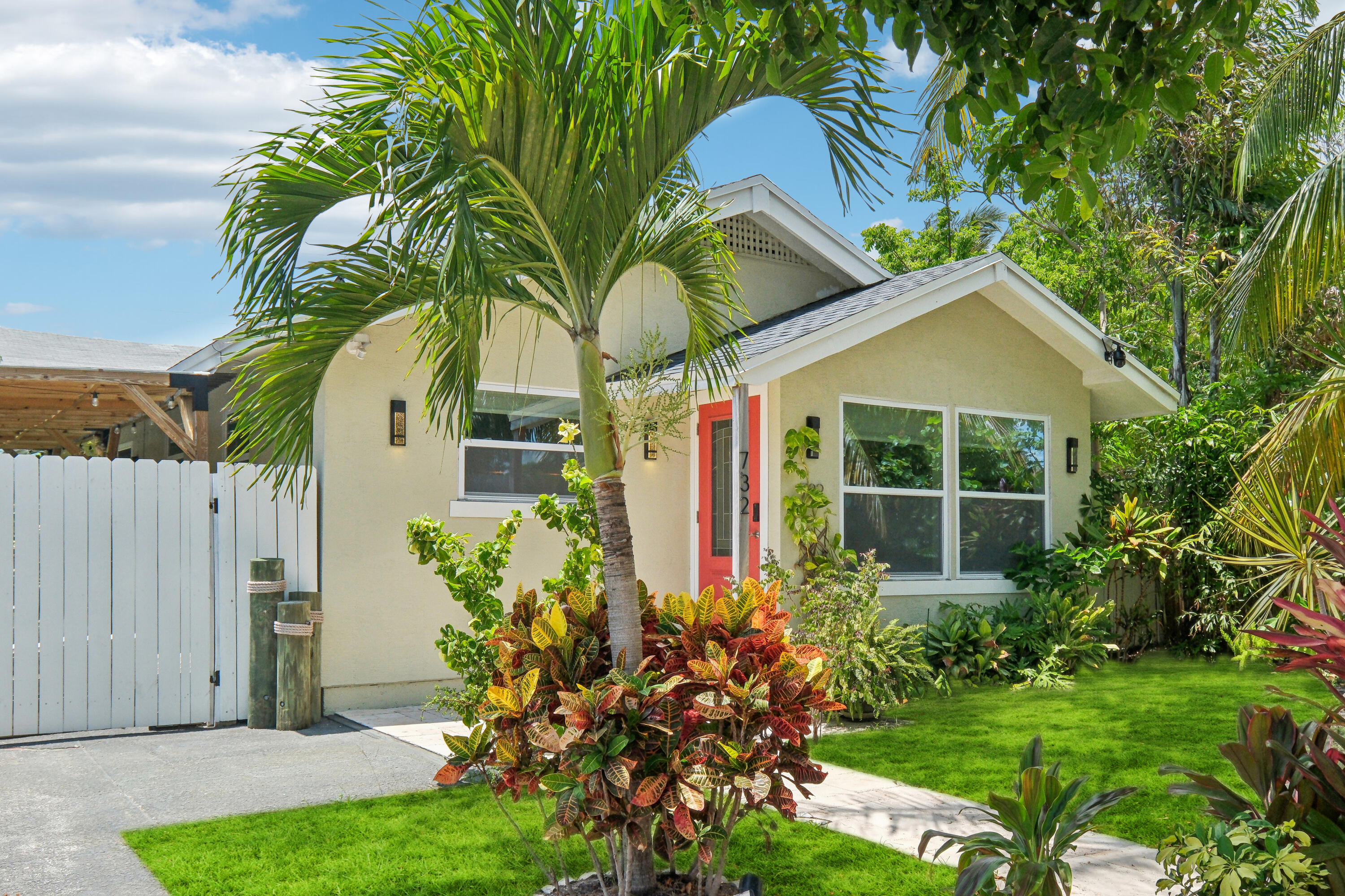 House exterior with a red front door, palm tree, and colorful tropical landscaping.