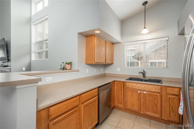 Kitchen with wood cabinets, light countertops, and a sink beneath a window with blinds.