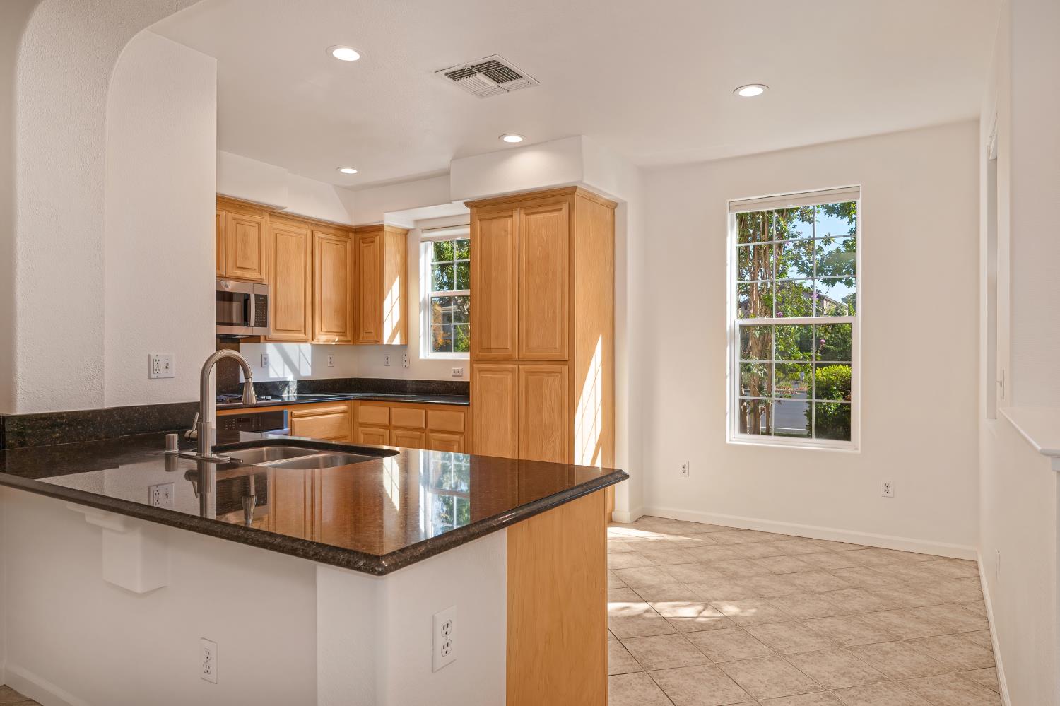 Kitchen with wood cabinets, dark granite counters, a large sink peninsula, and tiled flooring.