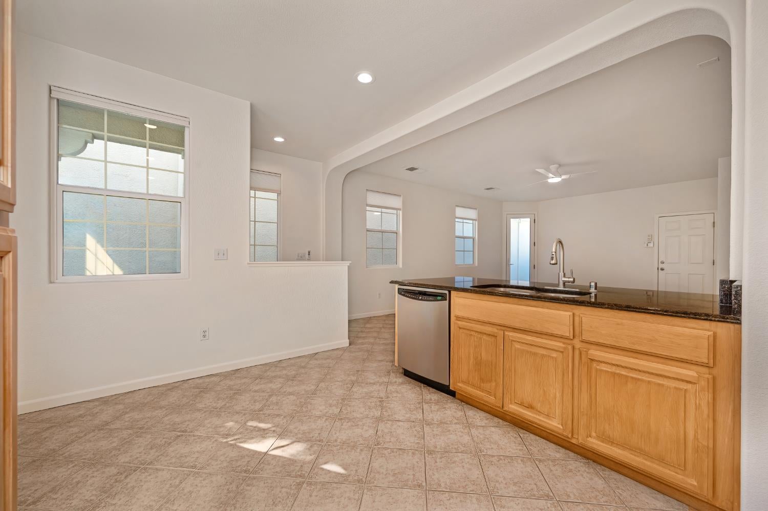 Kitchen with wood cabinets and a dark countertop island opening into a bright living area.
