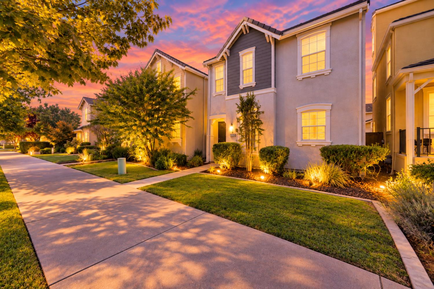 Two-story home with a landscaped front yard and illuminated windows at dusk.