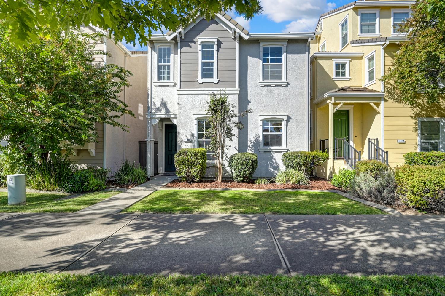 Gray two-story home with white trim, a dark green entry door, and landscaped front lawn.