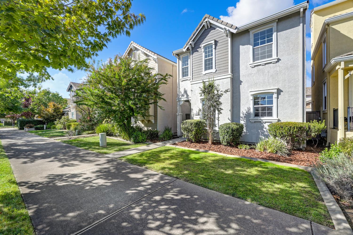 Two-story gray home with white trim, landscaped front yard, and curved concrete walkway.