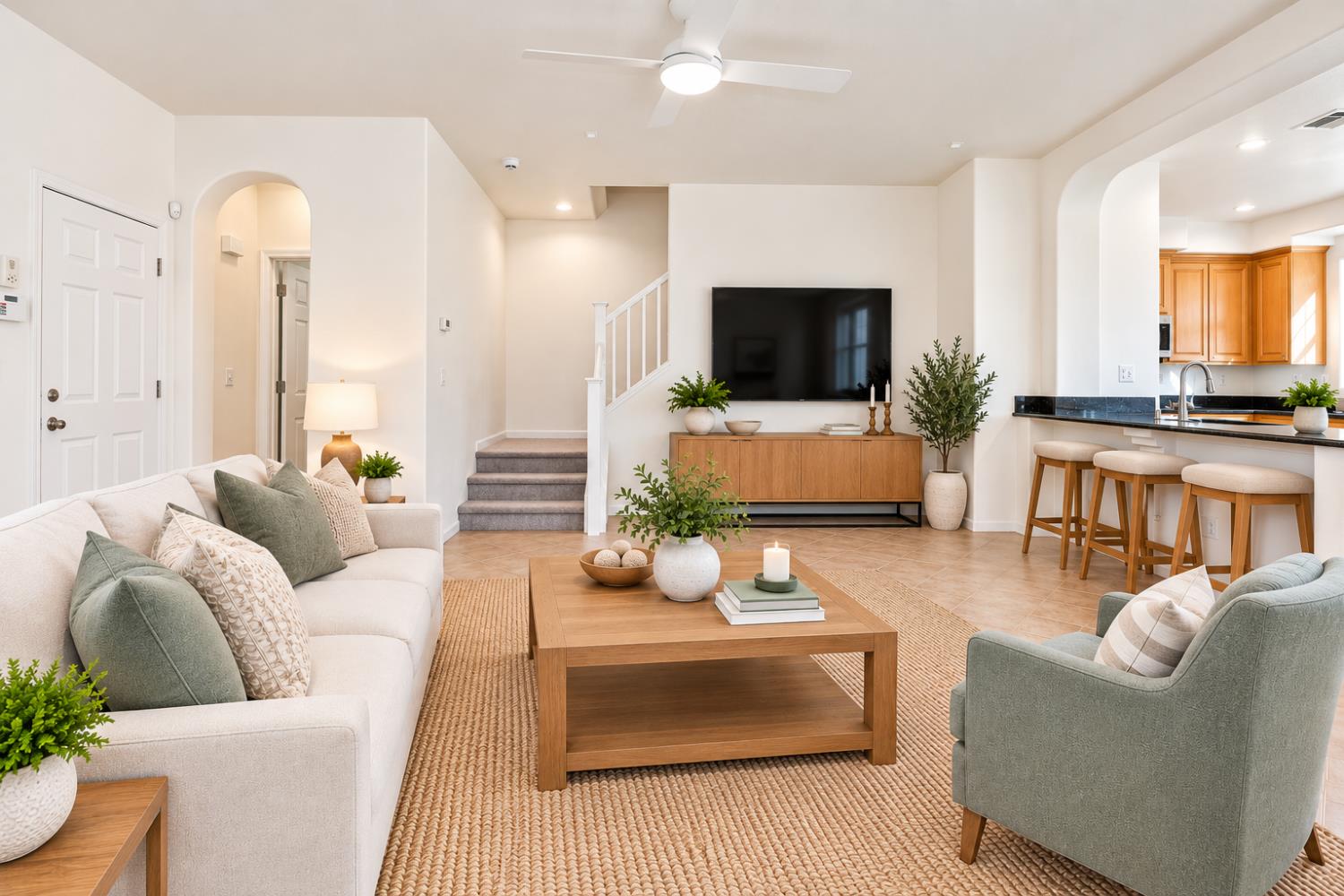 Furnished living room with a staircase, wall-mounted television, and open kitchen bar.