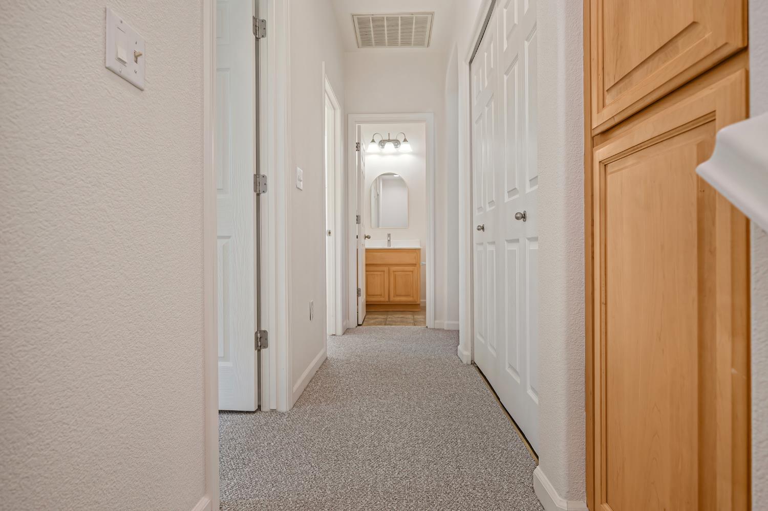 Carpeted hallway with light wood cabinets and a bathroom vanity visible at the far end.