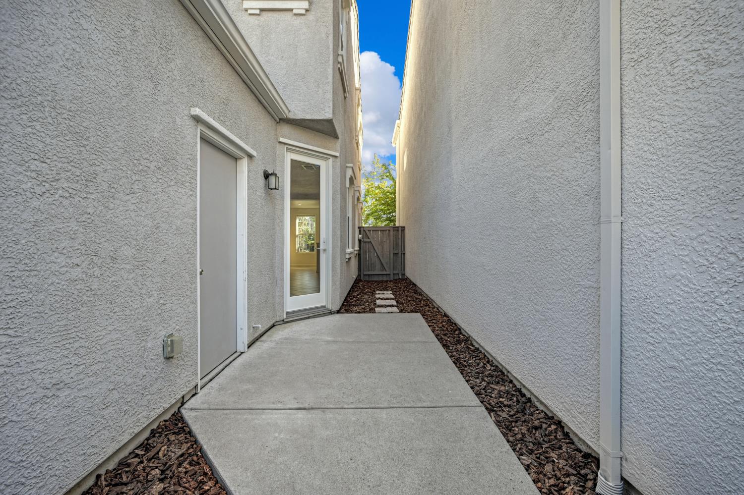 Concrete walkway between stucco walls leads to a wooden gate beside a glass door.