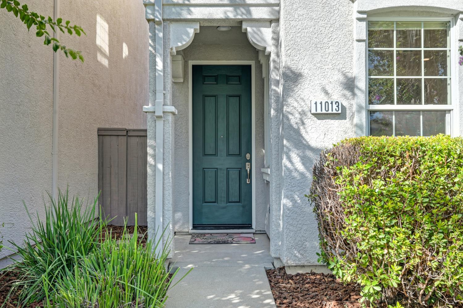 Front entrance with a teal paneled door, decorative stucco arch, and 11013 address plaque.