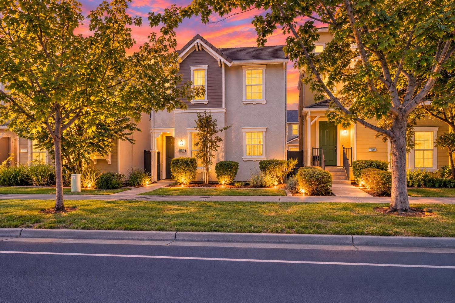 Two-story townhouse with lit windows and landscaped front yard beneath a colorful dusk sky.