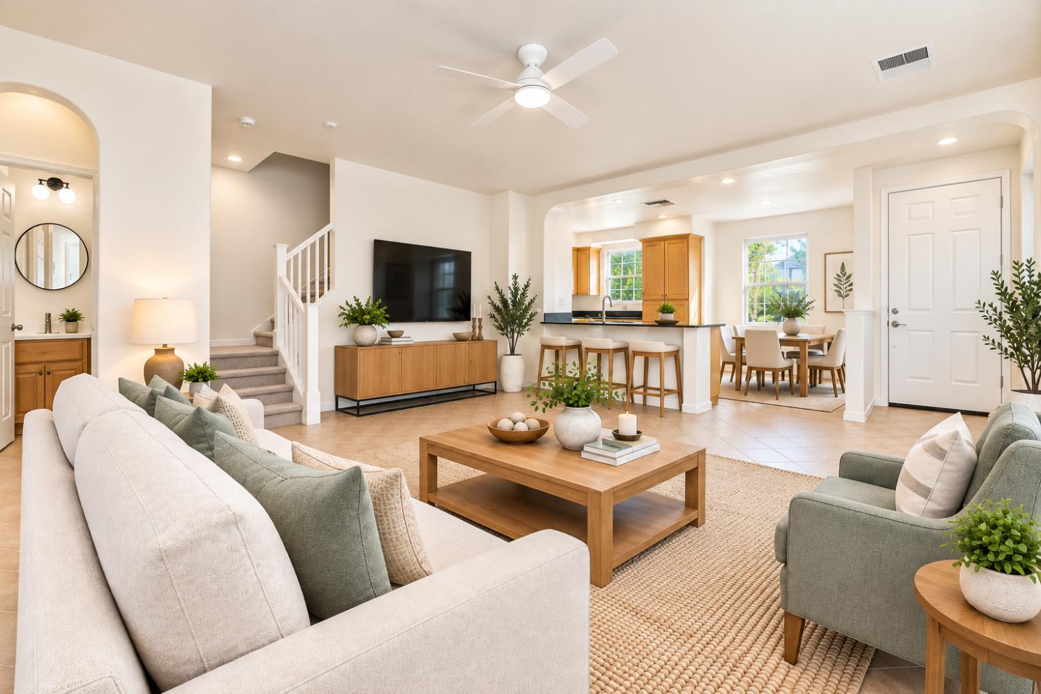 Open-plan living room with a wood coffee table, TV, staircase, kitchen island, and dining area.