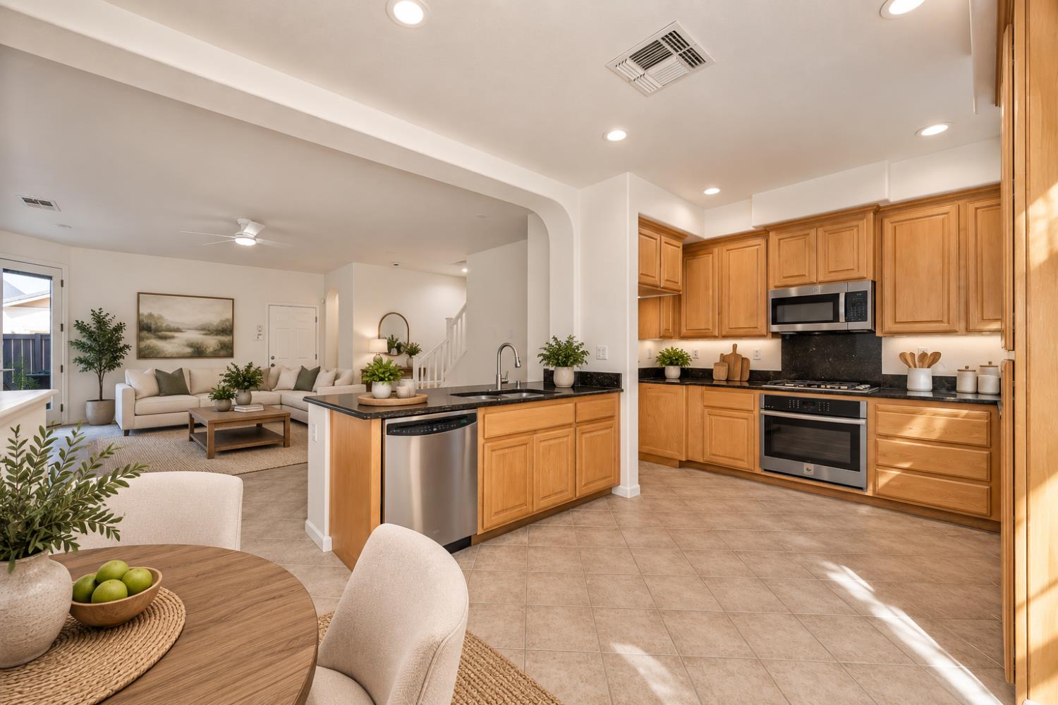 Open-plan kitchen with warm wood cabinets, black countertops, stainless steel appliances, and a central island.