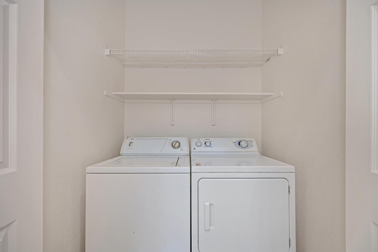 Laundry room with a white washer and dryer beneath wire shelving.