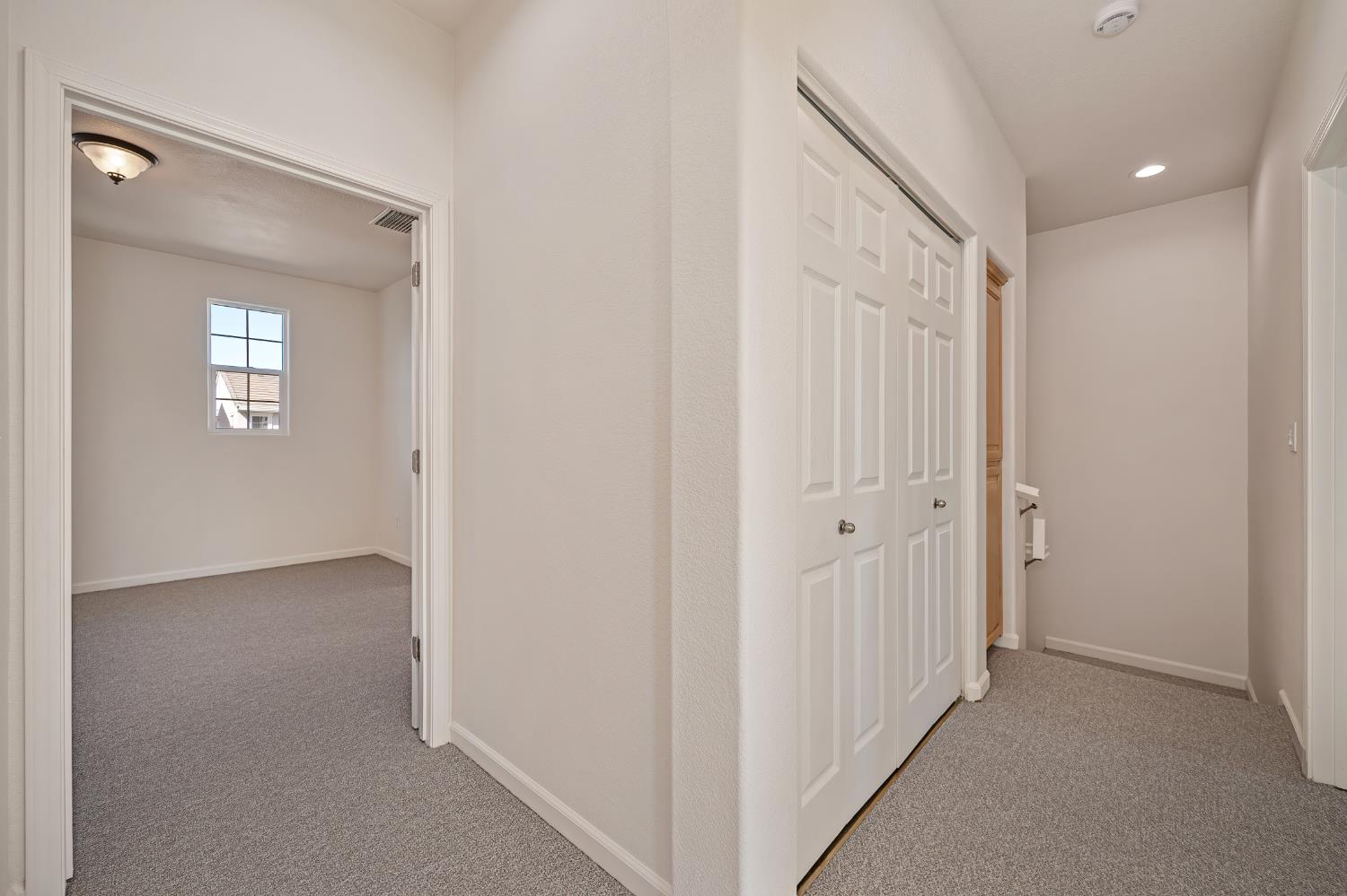 Carpeted hallway with paneled closet doors and an empty room visible through the doorway.
