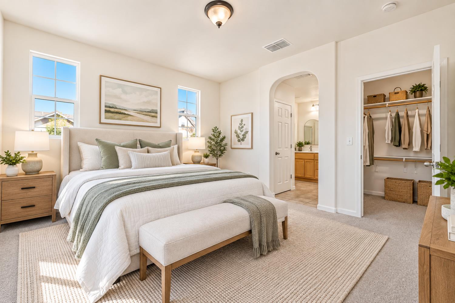 Staged bedroom with a white-and-sage bed, woven rug, open closet, and arched doorway to a bathroom.