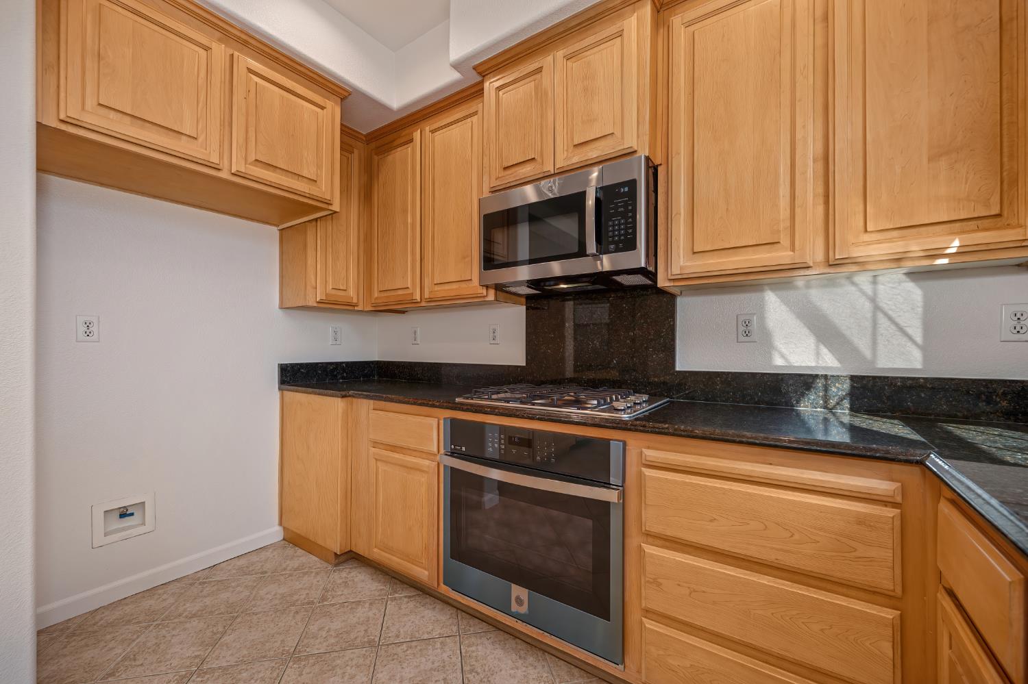 Kitchen with honey-colored wood cabinets, dark granite counters, and stainless steel appliances.