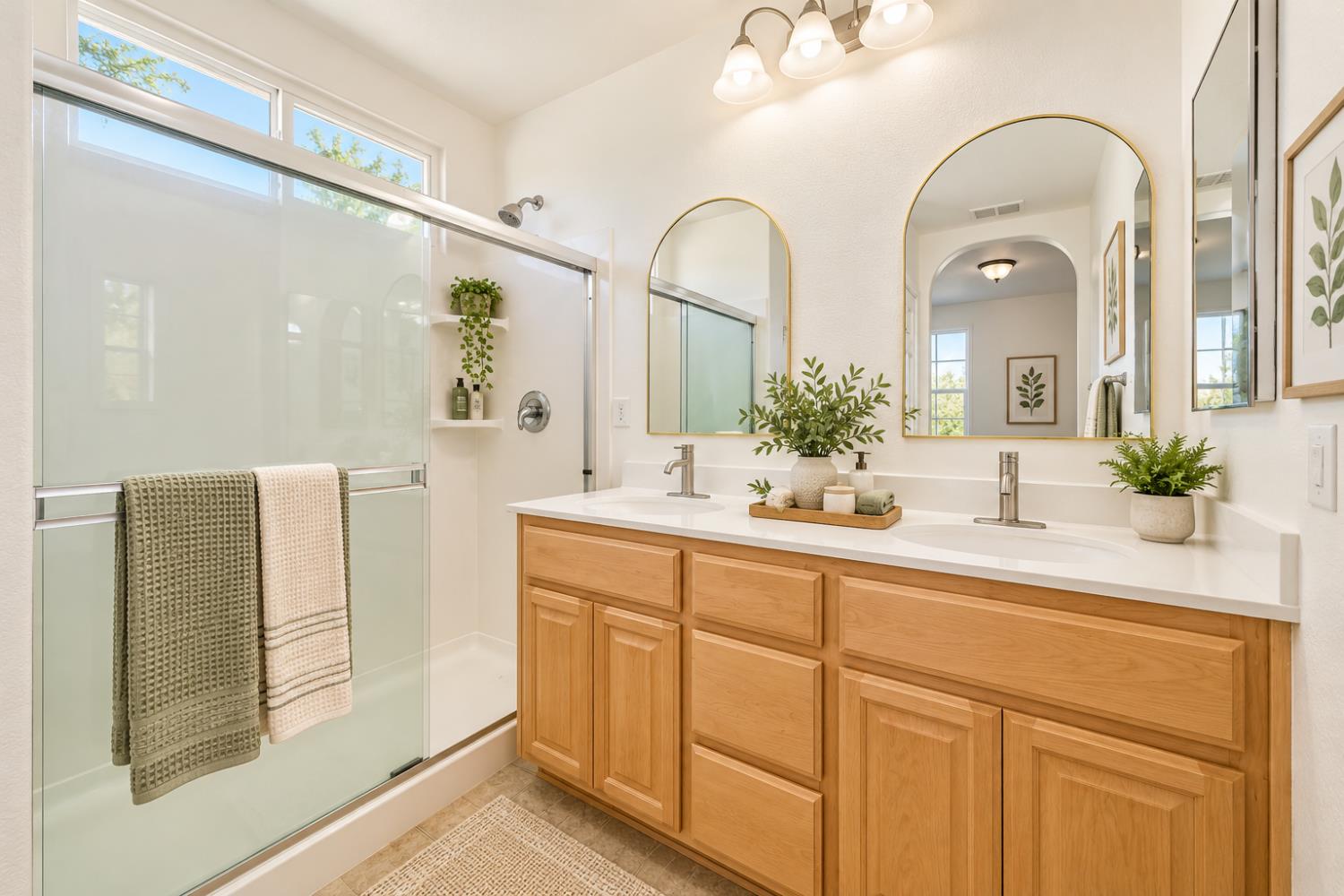 Bathroom with a glass shower, double vanity, and two arched mirrors.