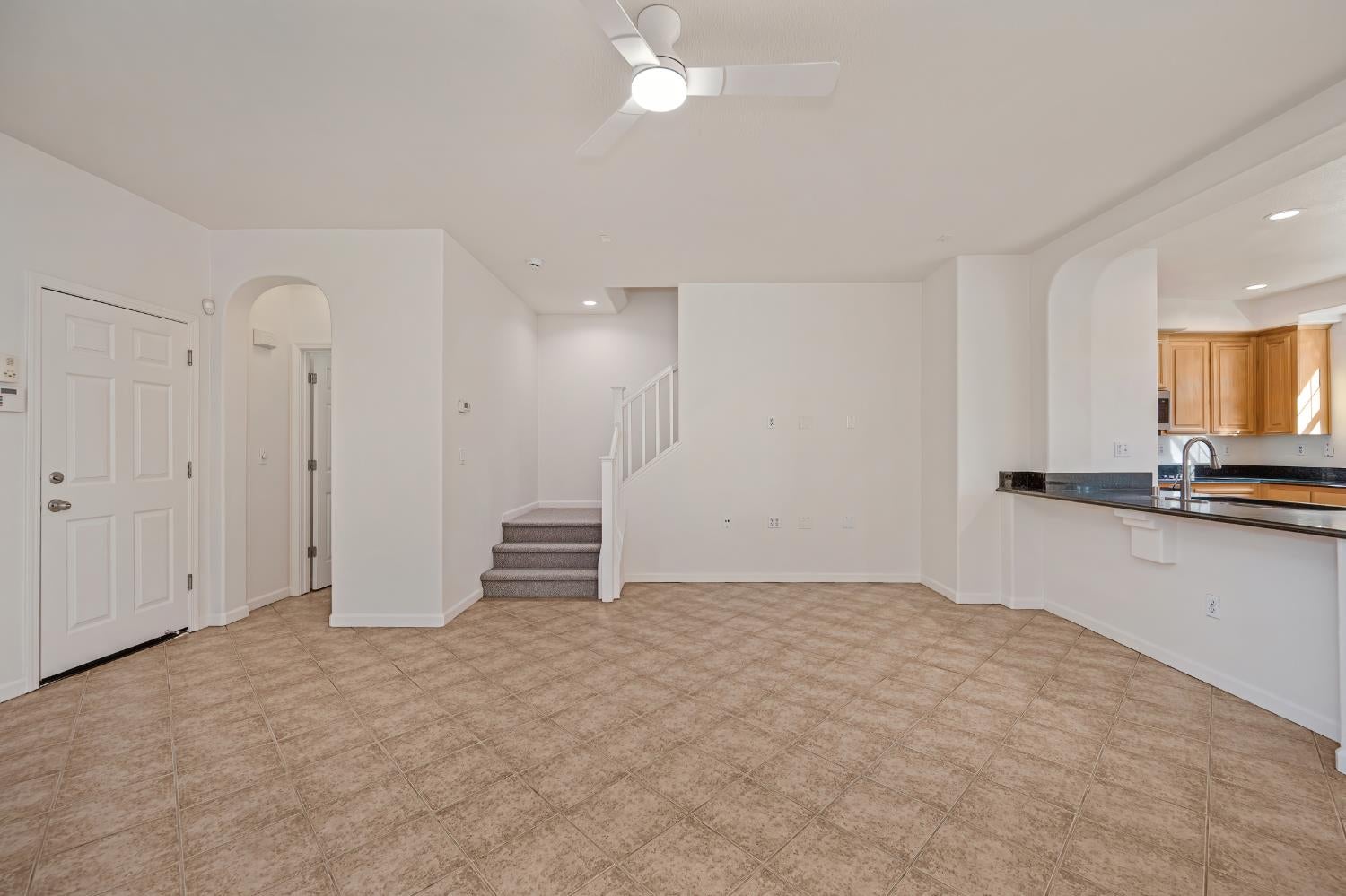 Open-plan living area with tan tile floors, a staircase, and an adjoining kitchen with wood cabinets.