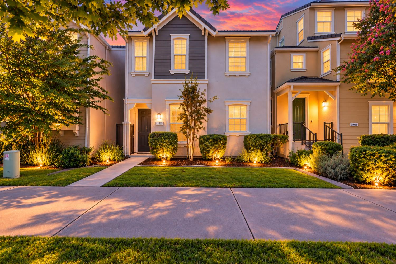 Two-story home at dusk with glowing windows, landscaped shrubs, and a front walkway.