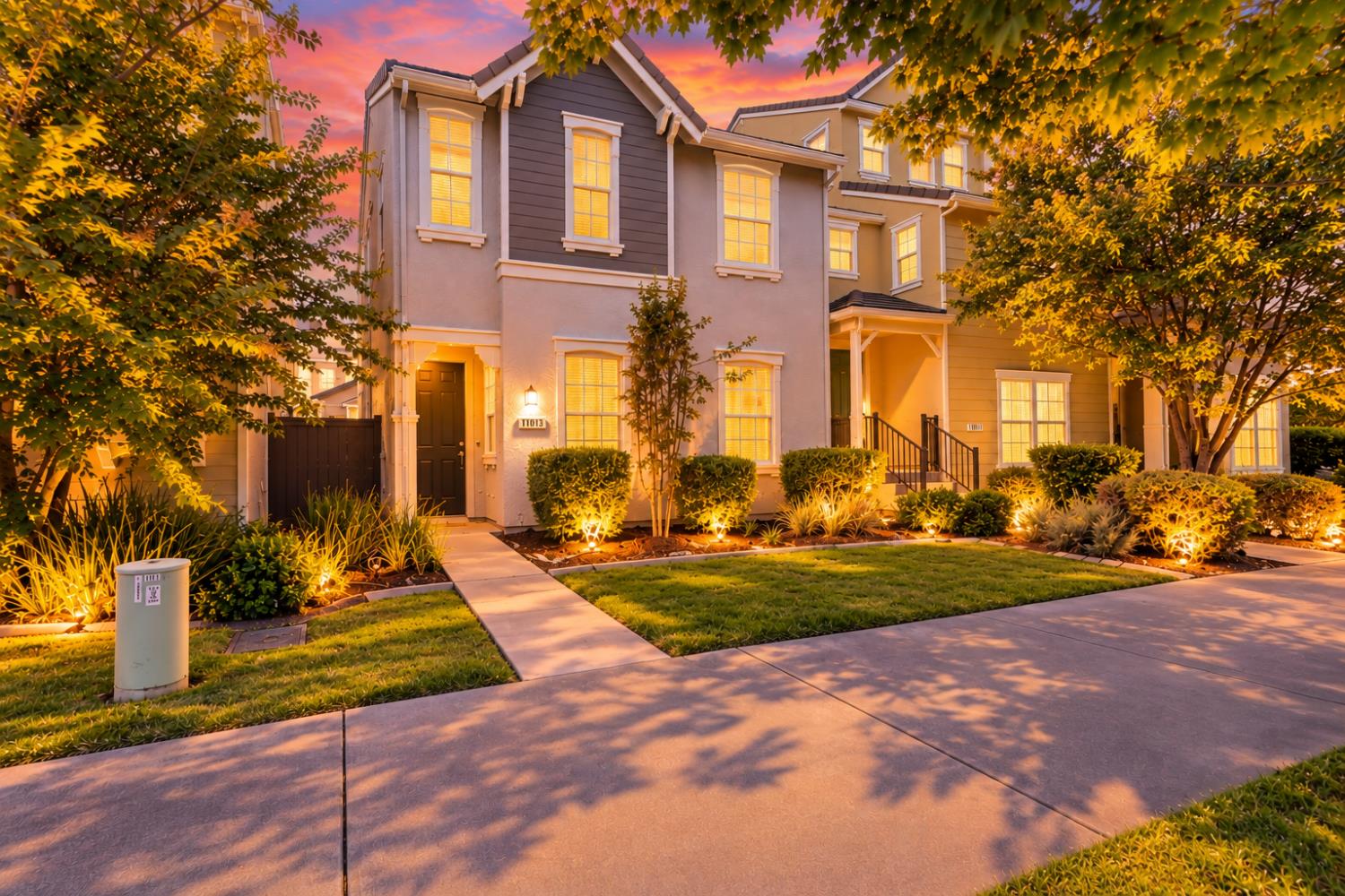 Two-story home with illuminated windows, landscaped front yard, and walkway at dusk.