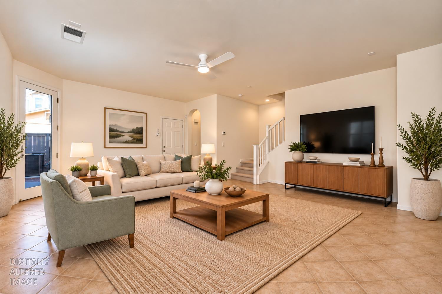 Staged living room with cream sofa, wood coffee table, large television, and staircase.