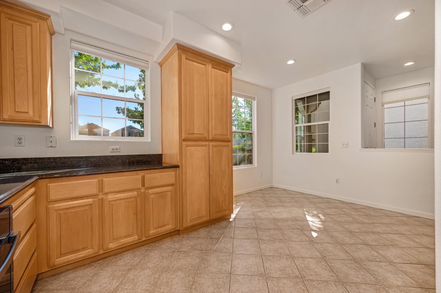 Kitchen with honey-colored cabinets, dark countertops, tiled floor, and large windows.