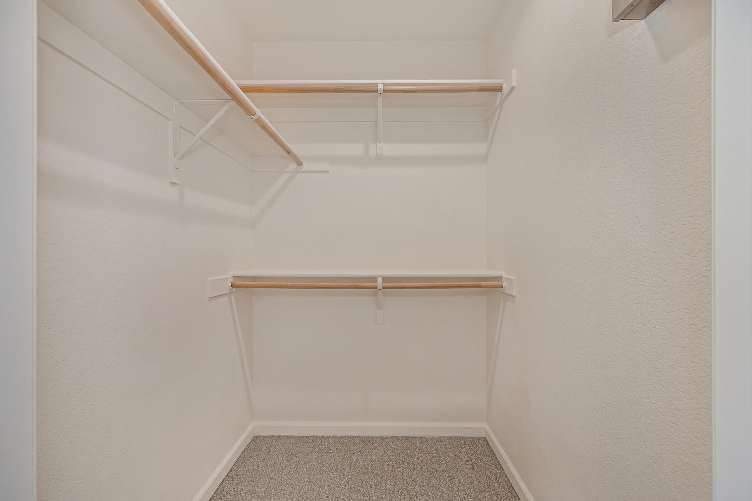 Empty walk-in closet with carpet and two levels of shelving and hanging rods.