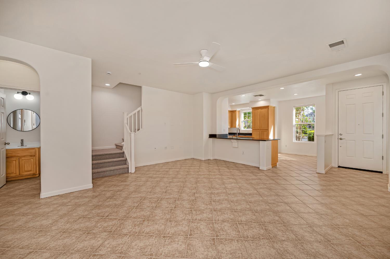 Vacant living area with tan tile floors, carpeted stairs, and an adjoining wood-cabinet kitchen.