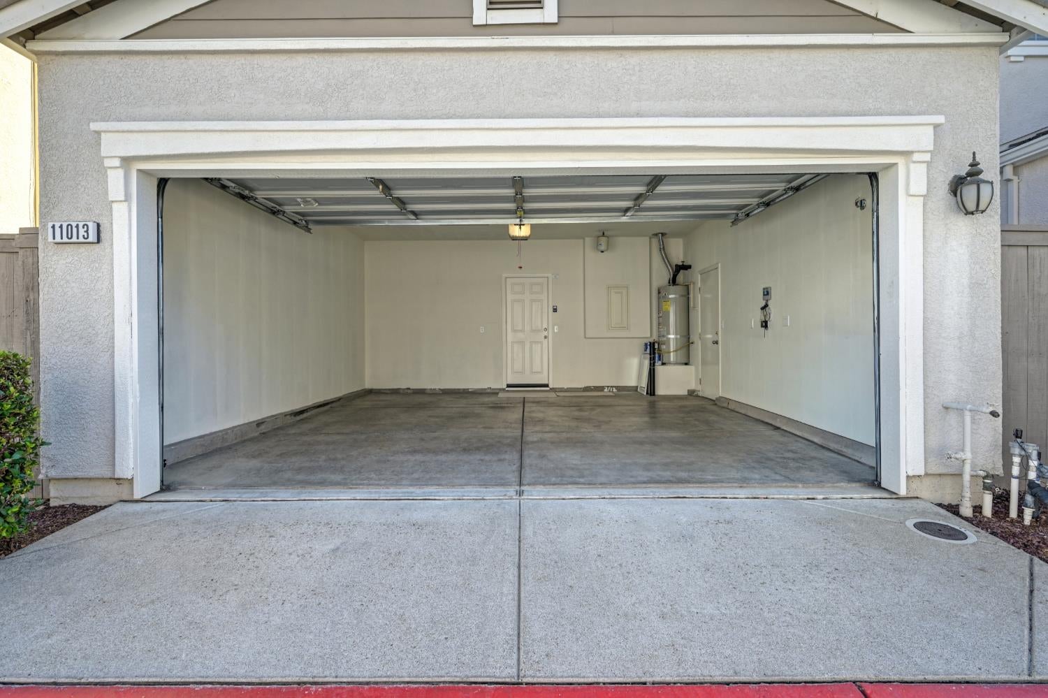 Open, empty two-car garage with a concrete floor and water heater at the back.