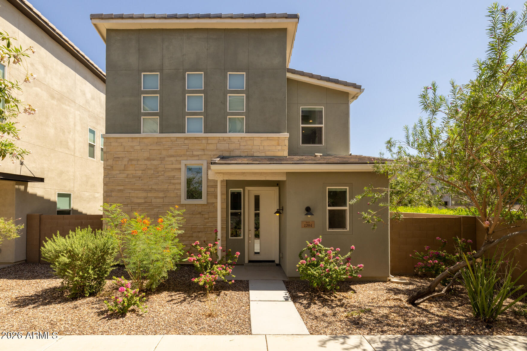 Modern two-story home with a stone facade, desert landscaping, and a walkway to the front door.