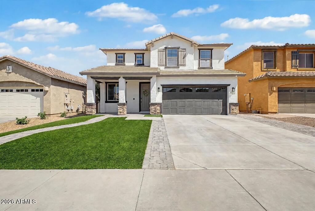 Two-story stucco home with a gray double garage, green lawn, and wide driveway.