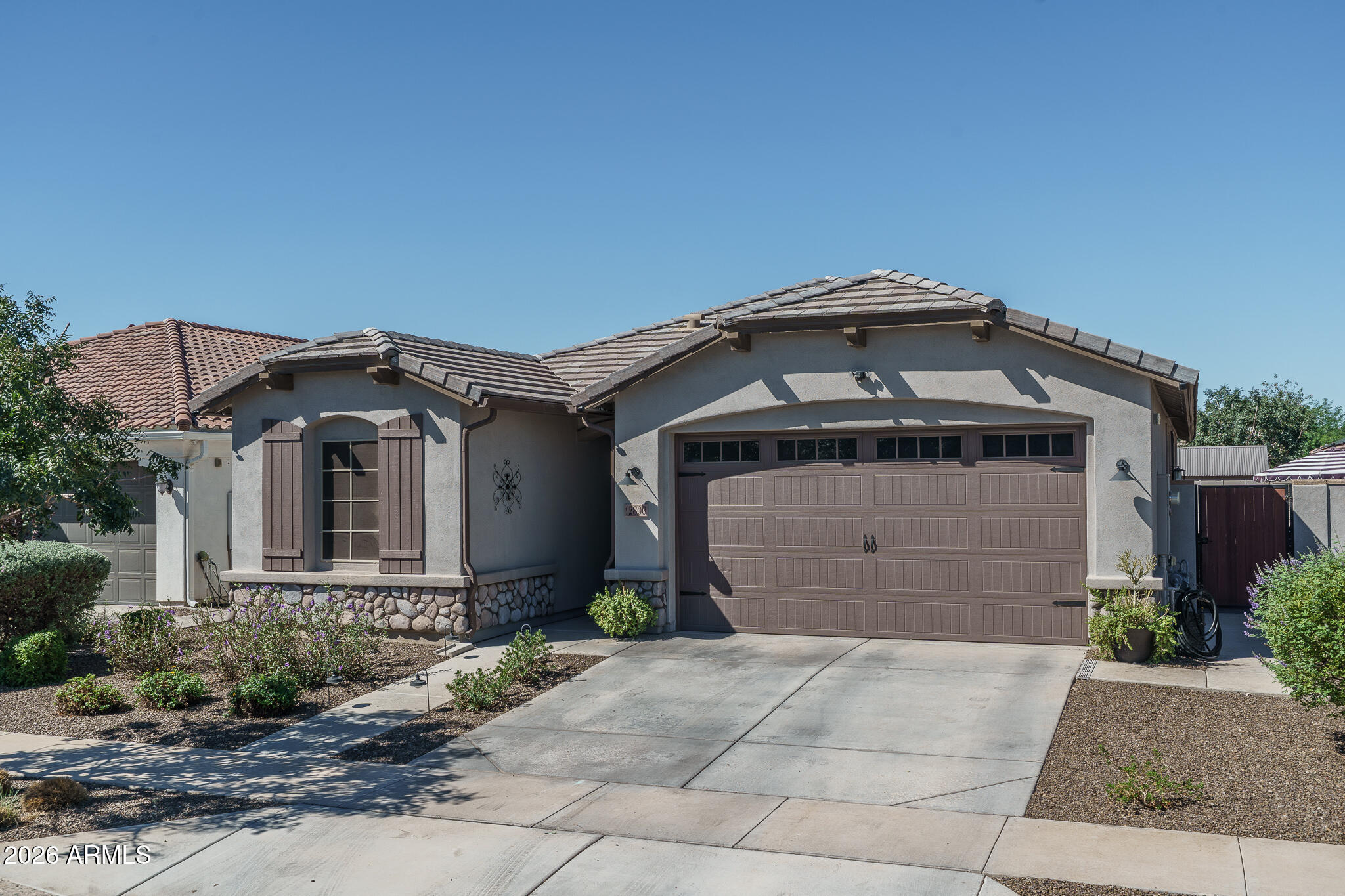 Single-story stucco home with a tile roof, stone accents, and a large brown garage door.
