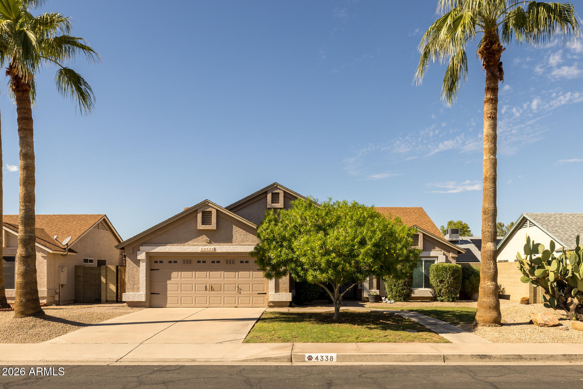 Stucco house with a two-car garage, palm trees, and desert landscaping.