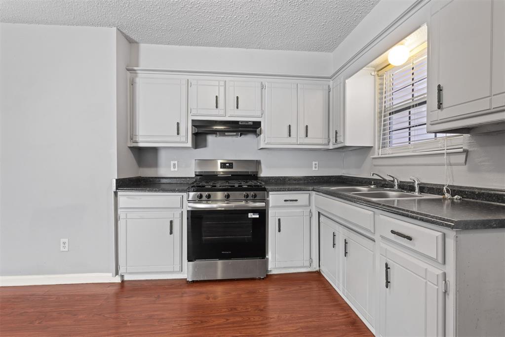Kitchen with white cabinets, dark countertops, a stainless steel range, and reddish wood flooring.