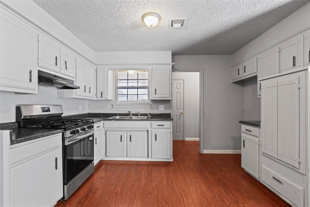 Kitchen with white cabinets, dark countertops, a stainless steel range, and reddish wood flooring.