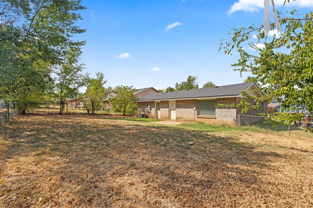 Single-story brick home beyond a broad leaf-strewn backyard, framed by mature trees.