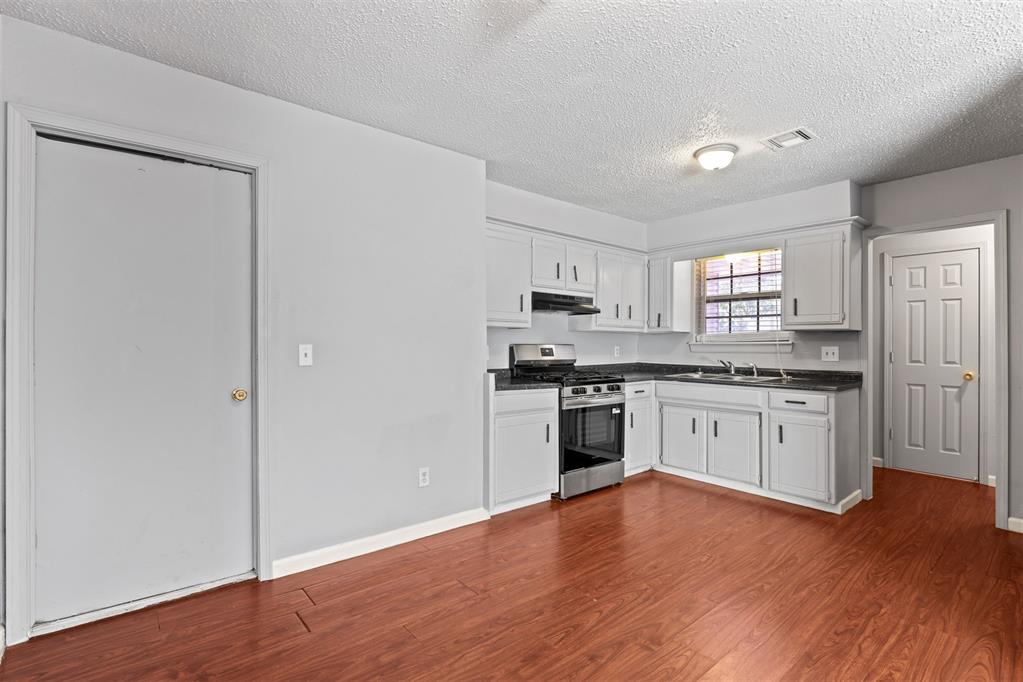 Kitchen with white cabinets, dark countertops, stainless steel range, and reddish wood-look flooring.