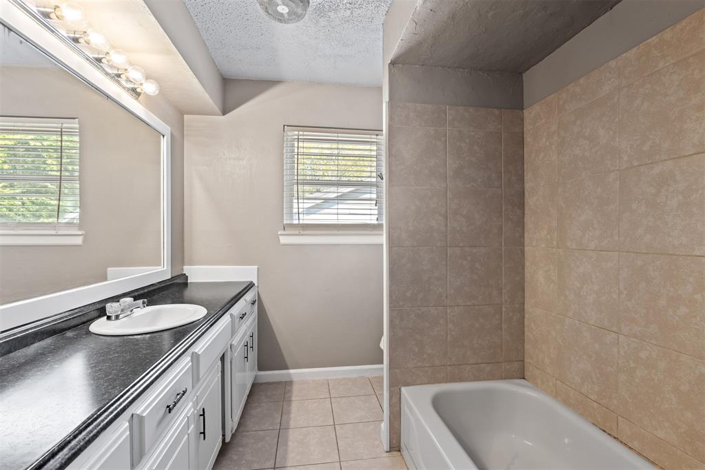 Bathroom with a black countertop vanity, large mirror, and tan-tiled bathtub surround.