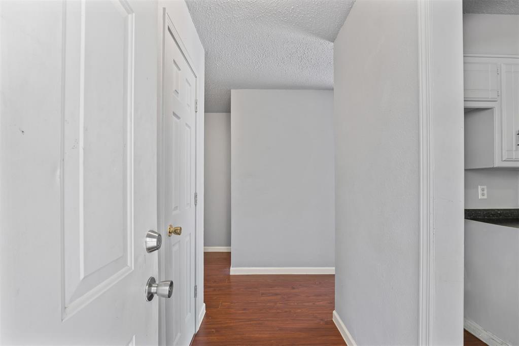 Interior hallway with reddish wood flooring, white paneled doors, and a glimpse of the kitchen.