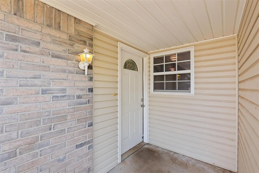 Covered front entry with a white door, window, beige siding, and brick wall.