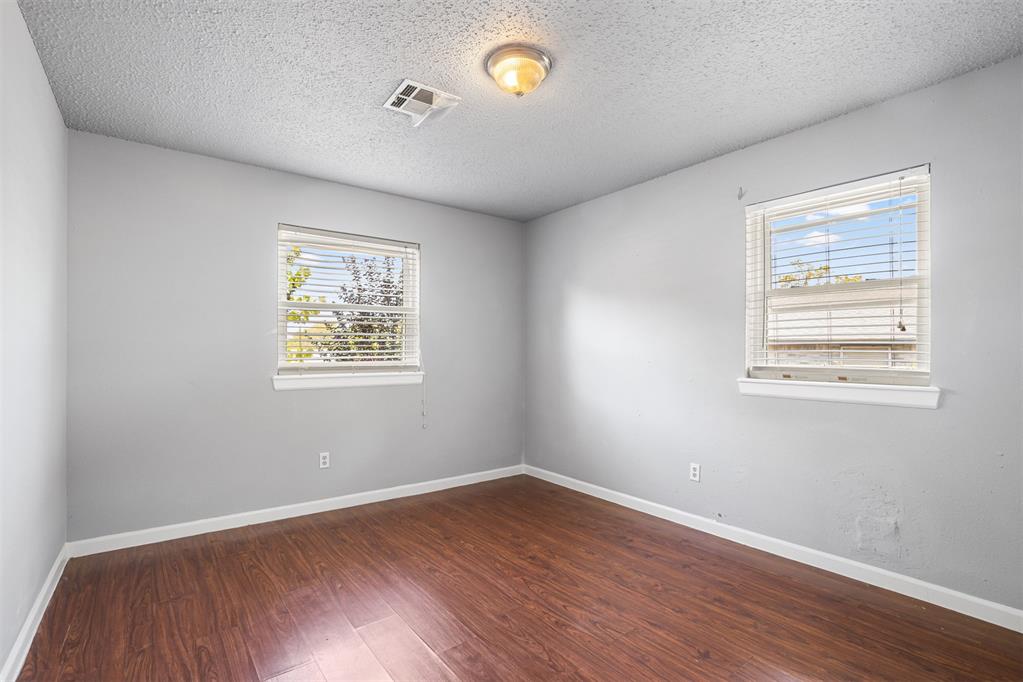 Empty bedroom with gray walls, wood-look flooring, and two windows with blinds.