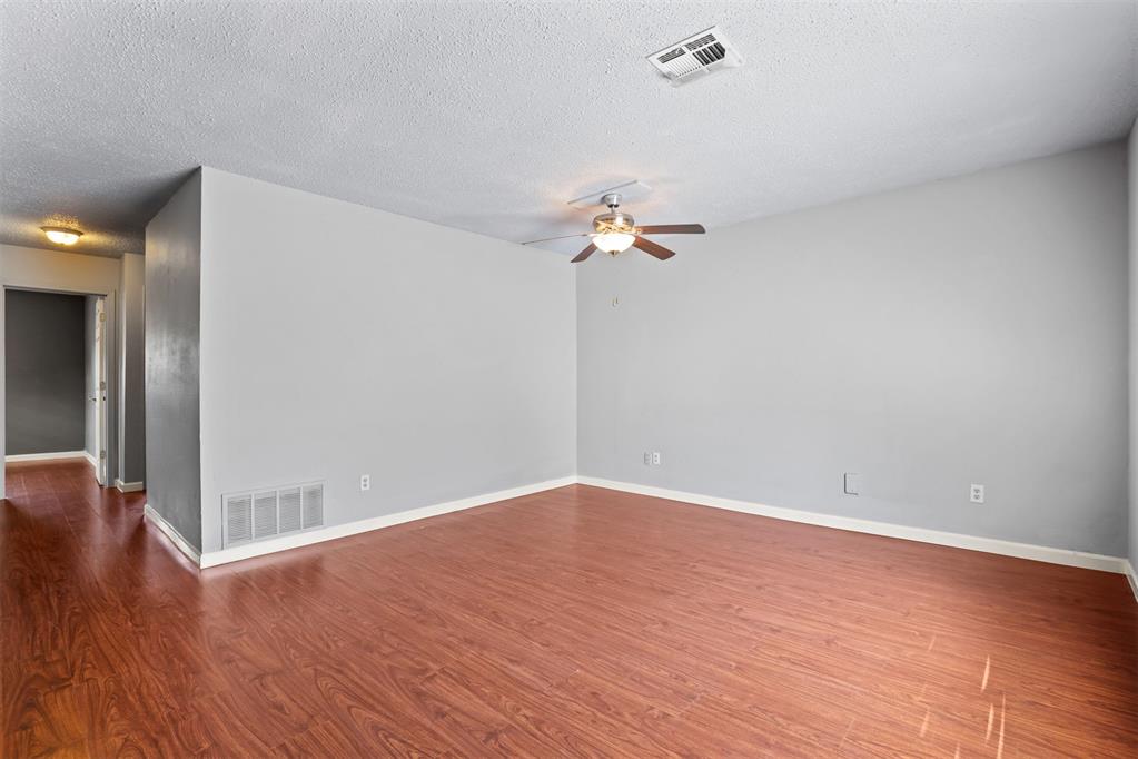 Empty living room with reddish wood-look flooring and a ceiling fan with light.