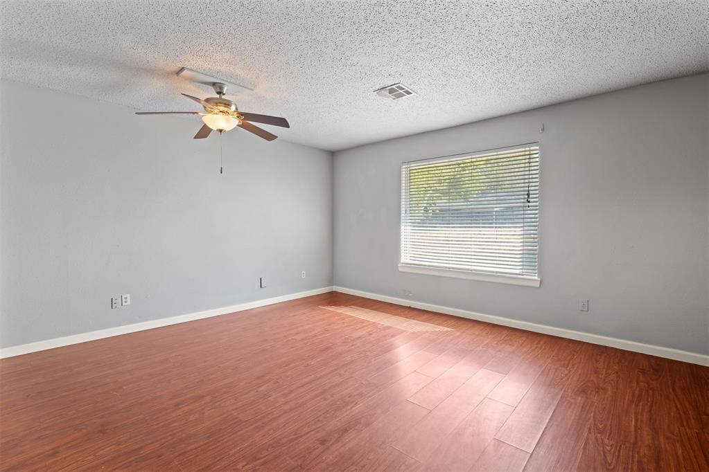Vacant room with reddish wood-look flooring, a ceiling fan, and a window with blinds.