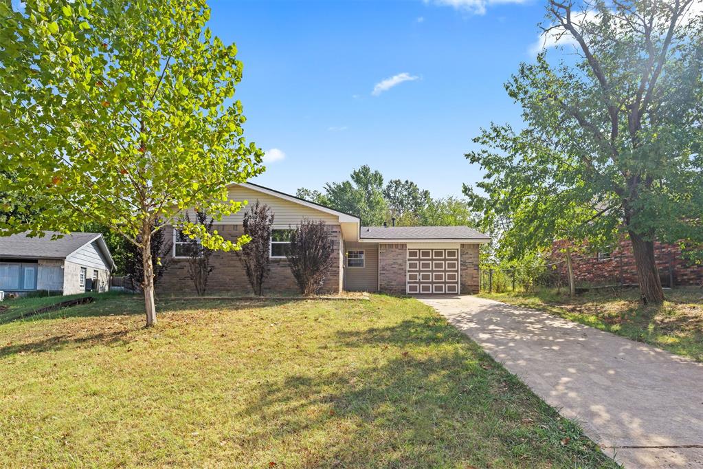 Single-story brick house with an attached garage, driveway, and mature trees.