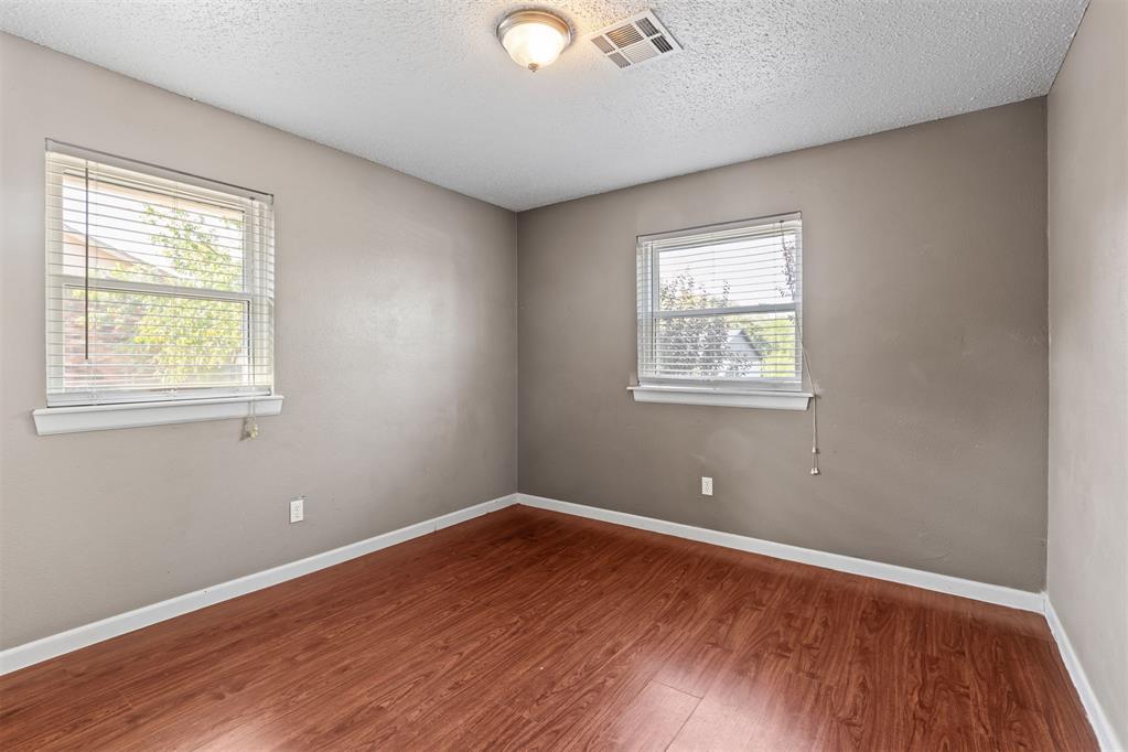 Empty room with reddish-brown flooring and two windows with white blinds.