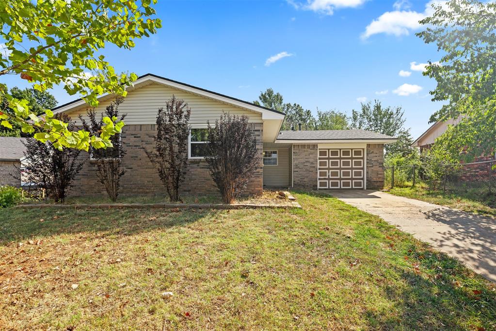 Single-story brick house with an attached garage, concrete driveway, and leafy trees in the front yard.
