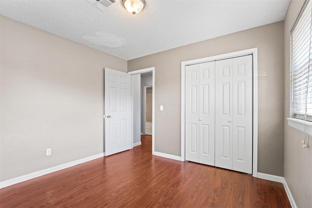 Empty bedroom with reddish wood-look flooring, a double-door closet, and an open bathroom doorway.