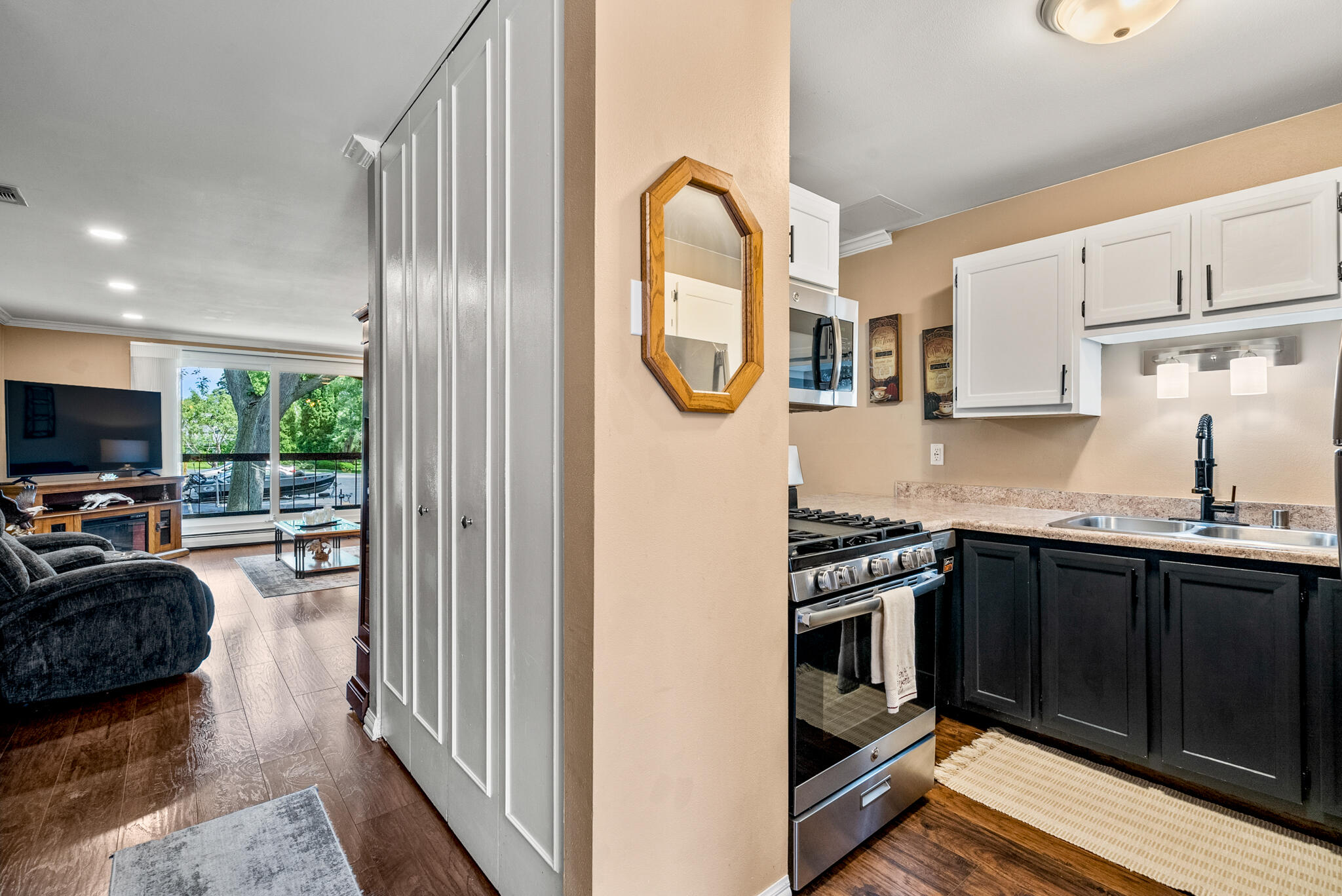 Kitchen with white upper cabinets and stainless-steel range, opening onto a living room with large windows.