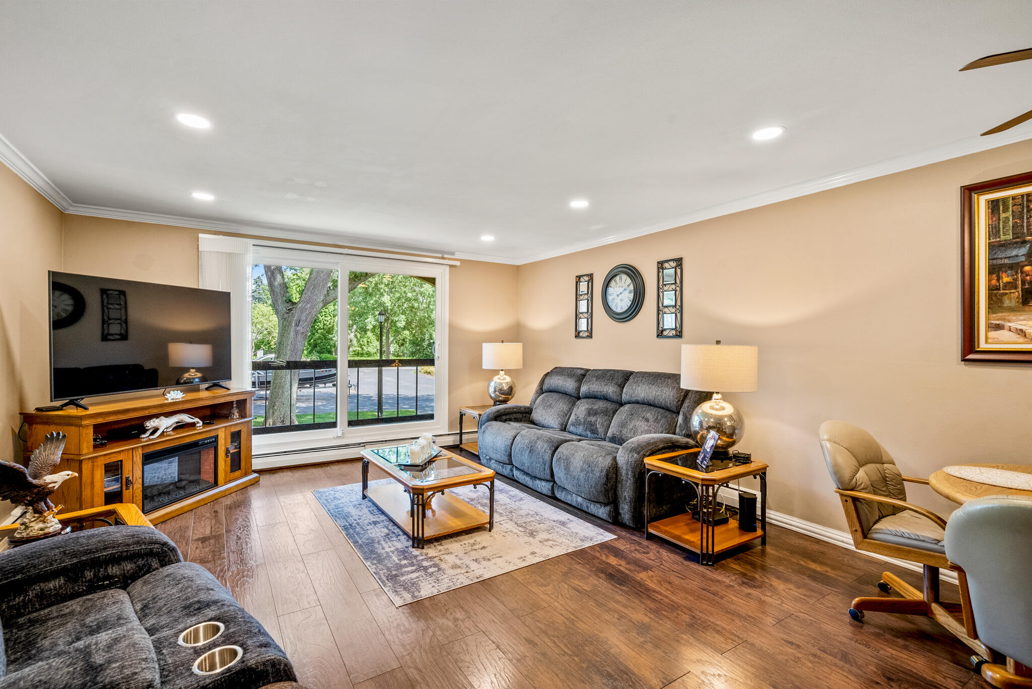 Living room with gray sofas, wood-look flooring, and sliding glass doors overlooking leafy trees.