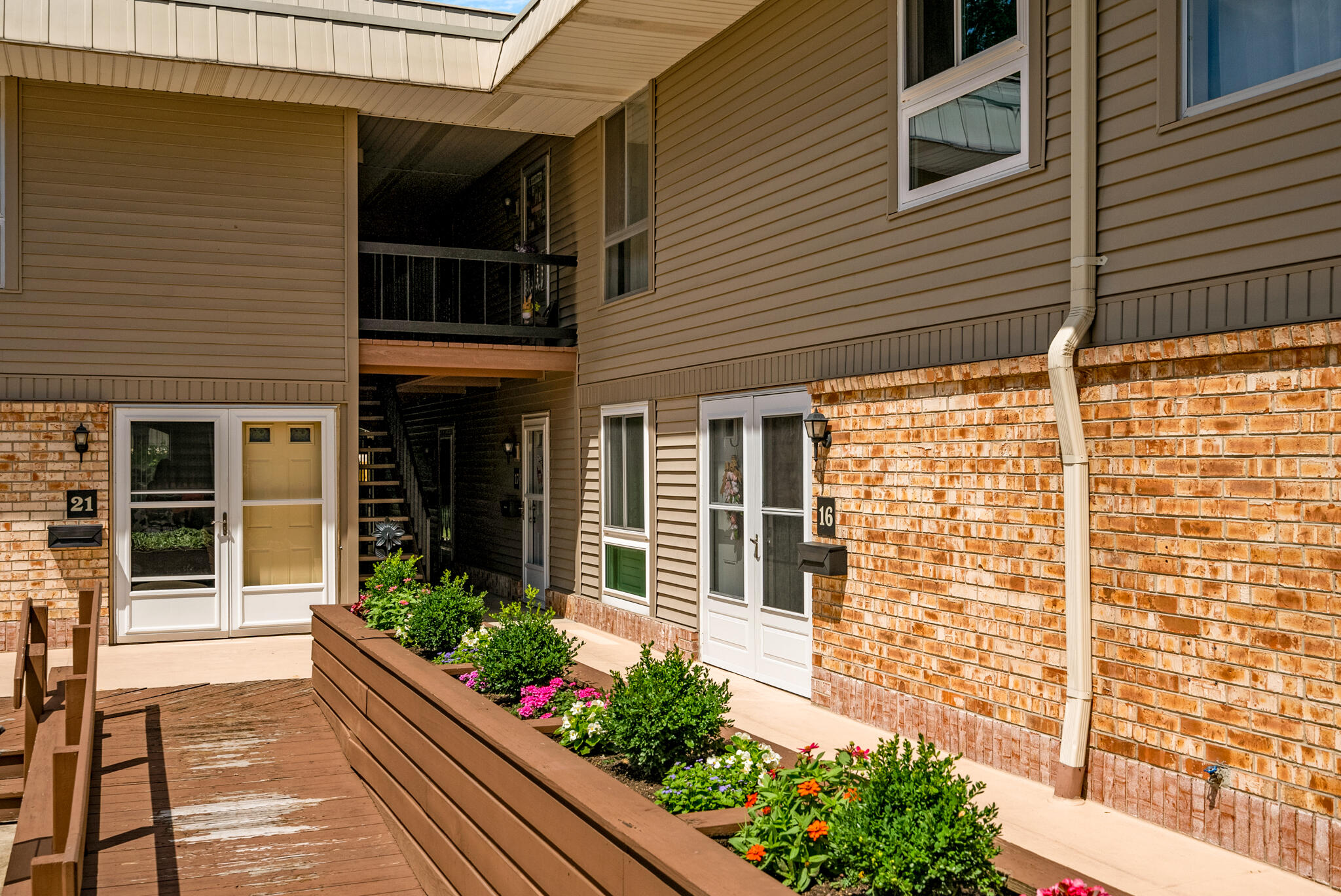 Residential entrance marked 16 beside a flower-filled raised planter and wooden walkway.